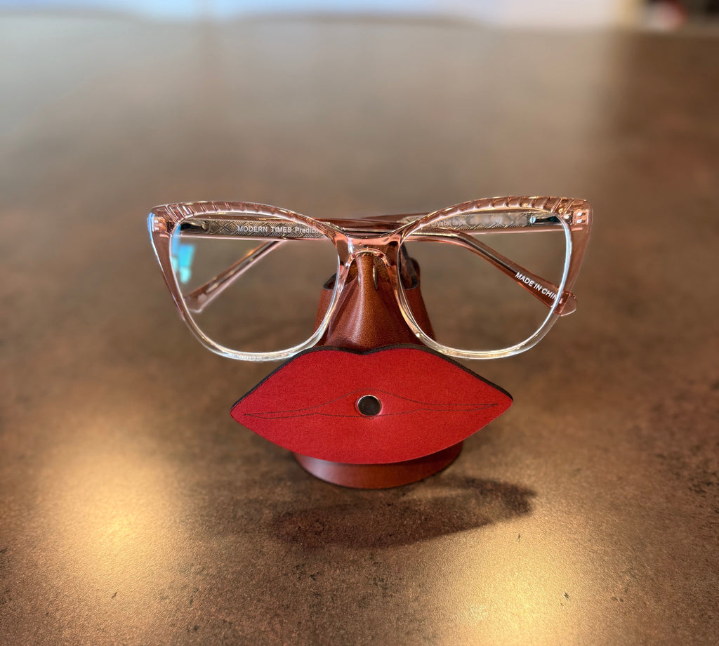 Red lip-shaped glasses holder with glasses on a reflective surface