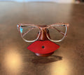 Red lip-shaped glasses holder with glasses on a reflective surface