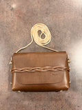 Brown leather handbag with braided handle on a textured surface
