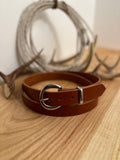 Brown leather belt with silver buckle on a wooden surface with blurred antlers in the background