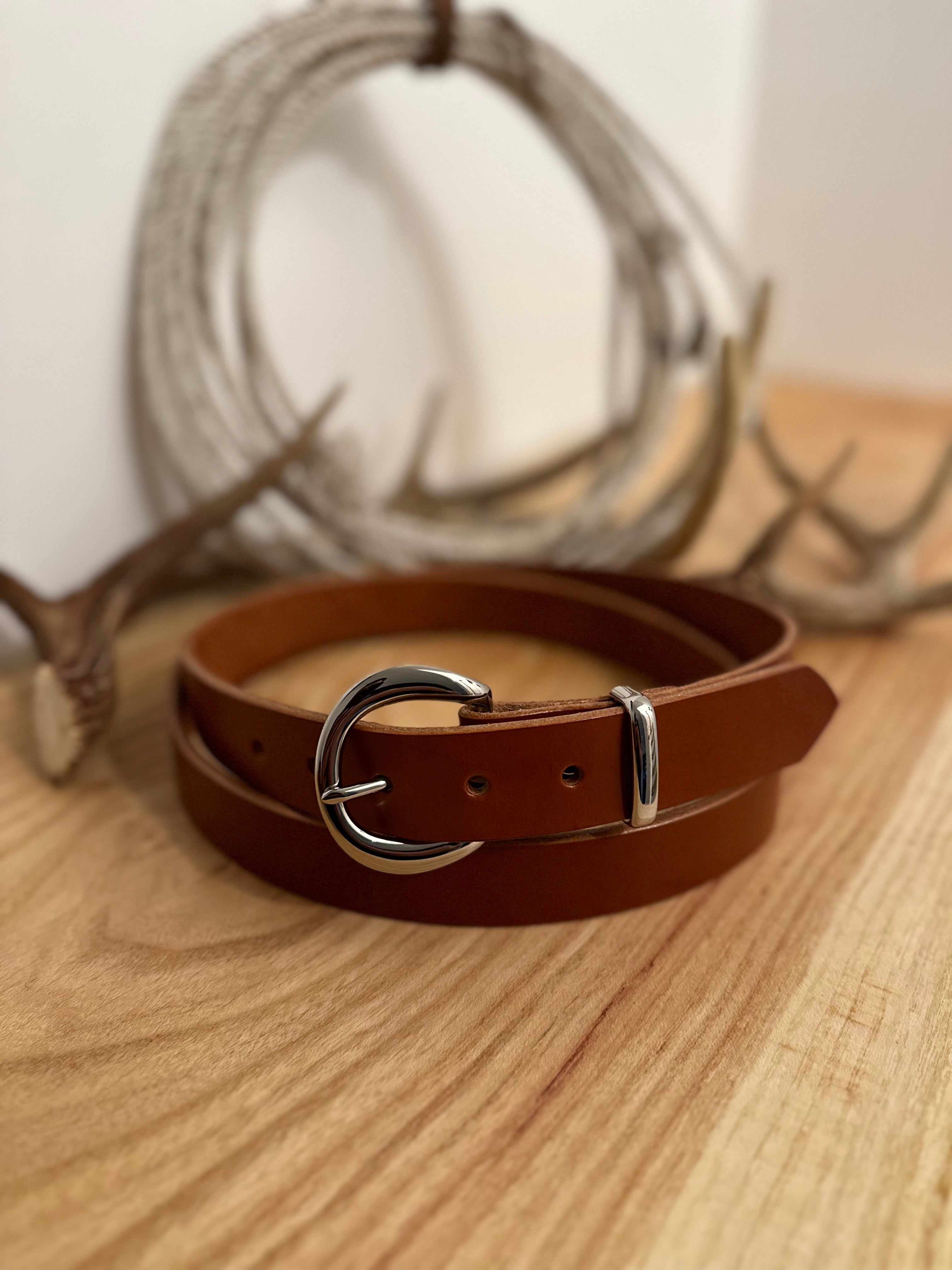 Brown leather belt with silver buckle on a wooden surface with blurred antlers in the background